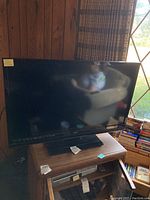 Photo of the full TV on stand showing screen and wood panel wall background.