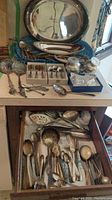 Full view of the silver plated platters and assorted cutlery laid out on table and inside drawer.