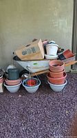 Wheelbarrow filled with various plastic flower pots, hanging planters, a few cardboard boxes, and a metal bucket next to it.