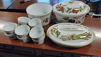 13 piece vintage bakeware lot including round and oval ceramic dishes with lids and eight ramekins, decorated with fruit and vegetable motifs.