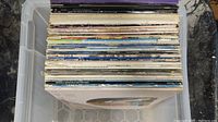 A large plastic bin filled with approximately 45 rock LP vinyl records, showing a side profile of the album spines with various artists and labels visible.