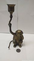 Front and side view of brass monkey candle holder next to a coin for size reference showing the detailed face and body.