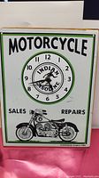 Front view of rectangular tin sign clock displaying 'MOTORCYCLE' at top, circular clock face with 'INDIAN GASOLINE' branding, a motorcycle graphic at bottom, and text 'SALES' and 'REPAIRS' on each side.