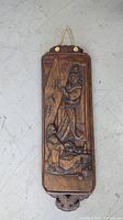 Full vertical view of carved wooden panel showing two figures and hanging hardware