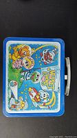 Top view of lunch box showing full-color Muppet Babies illustration with blue border and white handle.
