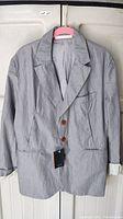 Full photo of light gray men's blazer on hanger showing front design, lapel collar, brown buttons, and pockets.