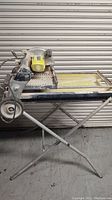 Full view of the Ryobi WS750L tile saw assembled on the folding and rolling stand, showing dust and dirt from prior use.