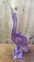Purple glass bird sculpture with elongated neck, standing on a square base, showing the front profile.