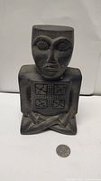 Front view of seated tribal statue with geometric patterns and coin for size reference.