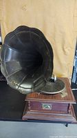 Front angle showing large black horn speaker, wooden base with RCA plaque and decorative pillars, and felt turntable.
