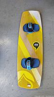 Top view of the yellow and white Liquid Force Overdrive wakeboard with blue bindings attached, showing the full length and design of the board.