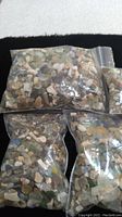 Four clear plastic ziplock bags containing small pieces of beach glass in multiple colors, mixed with sand, pebbles and shell fragments.