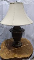 Front view of one lamp showing whole lamp with cream-colored bell shade and urn-shaped base in brushed brass finish.