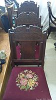 Set of four antique wooden chairs with carved wooden backs and floral embroidered upholstery on seat cushions in deep red fabric.