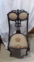 Front angled view of the antique wooden chair showing carved backrest and floral upholstered seat and backrest.