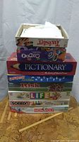 Stack of eight board games piled atop each other showing titles on the sides and tops of the boxes.