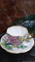 Square-shaped bone china cup with pink and yellow floral patterns and gold trim on the handle and rim.