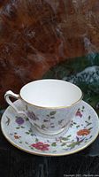 Fine bone china cup and saucer set with multicolored floral patterns and gold trim on a reflective surface