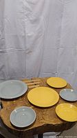 Six Fiesta plates in yellow and gray on wooden surface with white backdrop