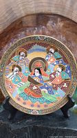 Full view of round ceramic decorative plate with five figures in colorful traditional robes and gold accents.