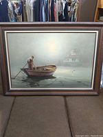 Full view of large framed painting depicting a man rowing a boat on misty water with lighthouse in the background.
