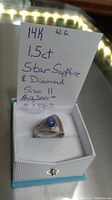 Ring displayed in its presentation box alongside handwritten note indicating 14k WG, 1.5ct star sapphire & diamond, and size 11