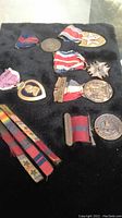 Full view of most medals laid on dark fabric, showing various pins, ribbons, and medals including purple heart, star-shaped medals, and round service medals.