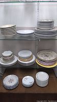 Wide view of shelves with various stacks of plates showing different sizes, patterns, and colors including white with blue rim, floral and gold rimmed plates.