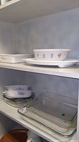 Shelf showing several baking dishes including white ceramic dishes with designs, blue patterned bowls, and clear glass baking dishes