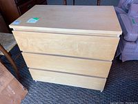 Front view of light wood finish dress with three drawers, showing minor wear and flat top surface