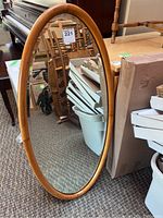 Full view of the oval mirror leaning against furniture, showing its size and wood frame.