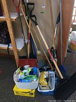 Wide view showing shovels, brooms, vacuum, and baskets with cleaning supplies and garbage bags.