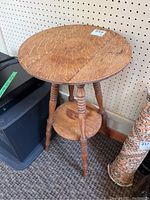 Round wooden plant table with visible wear, showing turned legs and lower tier shelf from side angle