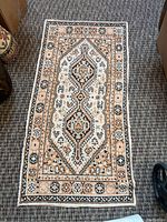 Full view of the rectangular rug showing the muted beige, peach, black and white geometric central pattern and decorative border.
