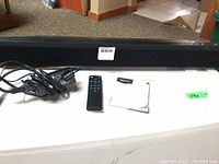 Full view of the Amazon Basics Bluetooth Sound Bar showing the sound bar, remote control, power cord, and manual on a white surface.