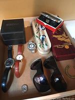 Photo showing four wristwatches, two pairs of sunglasses, two decorative trinket boxes and opera glasses with case.
