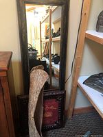 Framed wall mirror partially visible behind a framed metal wall art and bark canoe, showing the size and frame details of the mirror.