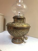 Full view of the brass oil lamp showing the ornate embossed patterns and clear glass hurricane.
