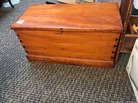 Closed view of linen chest made of solid wood with dovetail joints visible at corners, metal hardware latch on front, and a warm natural finish.