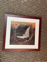 Full view of framed print on carpeted floor showing the wood frame and the colorful print depicting a waterfall and forest scene.