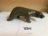 Side view of polished olive-green soapstone polar bear sculpture on table