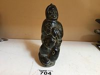 Front view of soapstone carving showing the seated Inuit woman holding a seal with facial features and parka detail.