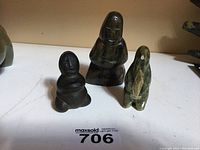 Three soapstone Inuit carvings showing the penguin figure, smaller and larger Inuit kneeling figures from front view.
