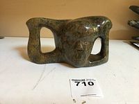 Front view showing polished green soapstone carving of a stylized human head with negative-space openings on both sides.