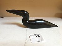 Side view of the dark polished soapstone bird carving showing its smooth, streamlined shape and detailed etching around neck and body.