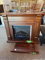 Front view of brown wood-look MDF fireplace surround with built-in electric fireplace insert. Detached baseboard with visible scratches lies in front.