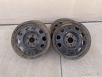 Four used 17 inch steel rims with visible rust and weathering, shown stacked in pairs on a cement floor.