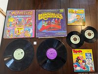 Photo showing 4 vintage children's vinyl records with their respective colorful illustrated storybook sleeves and booklets including Wizard of Oz and 6 Favorite Stories, Bedknobs and Broomsticks, Casper, and Popeye. Records laid out beneath the sleeves.