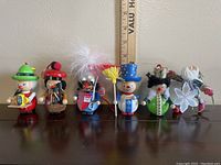 Photo showing the full set of five colorful handmade wooden ornaments with various characters lined up in a row, capturing their size against a ruler in the background.