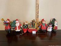 Photo of 7 assorted House of Hatten Denise Calla holiday ornaments arranged in a row with a ruler in the background for size reference.